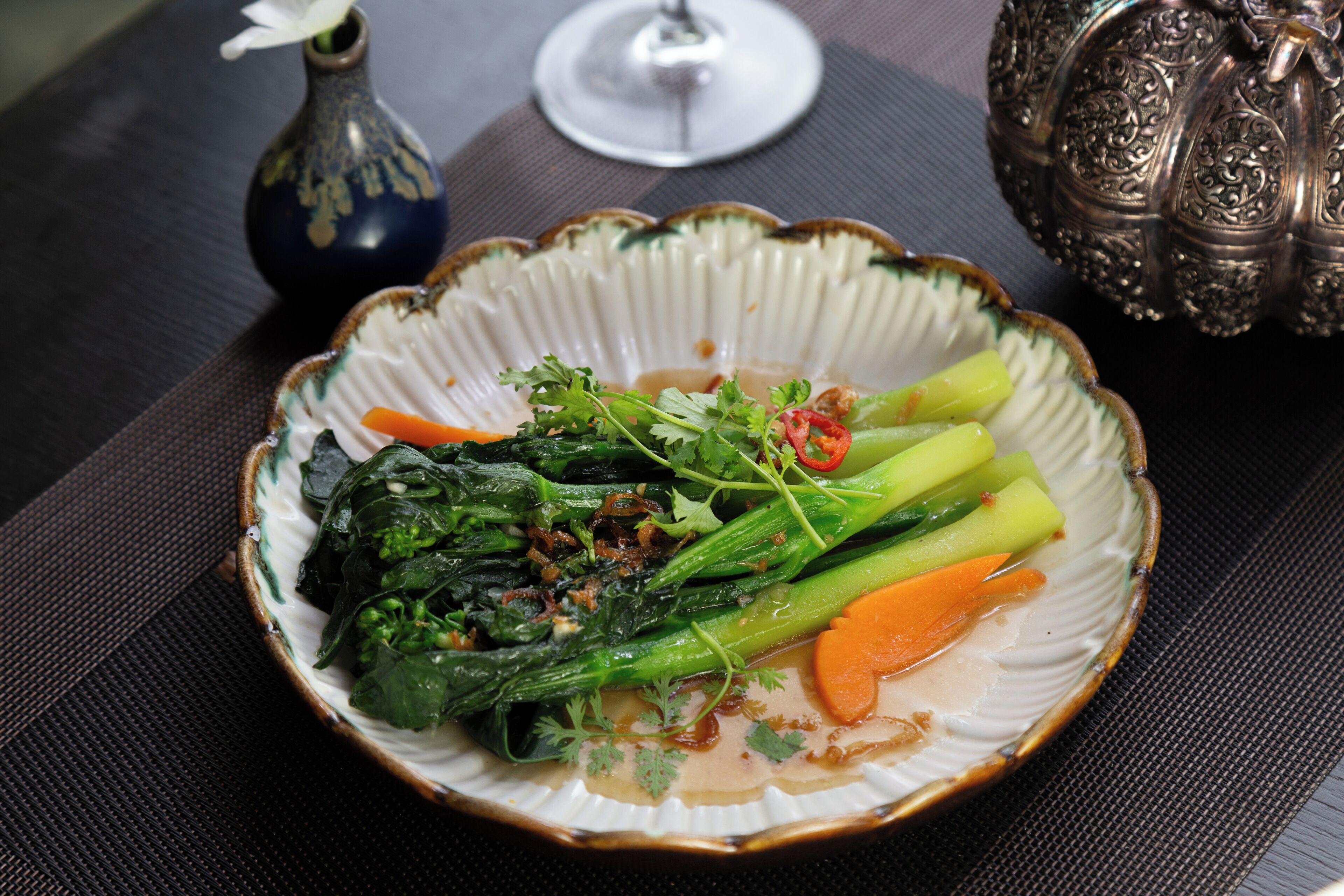 A plate of stir-fried vegetables with a decorative bowl and a glass of water on a table.