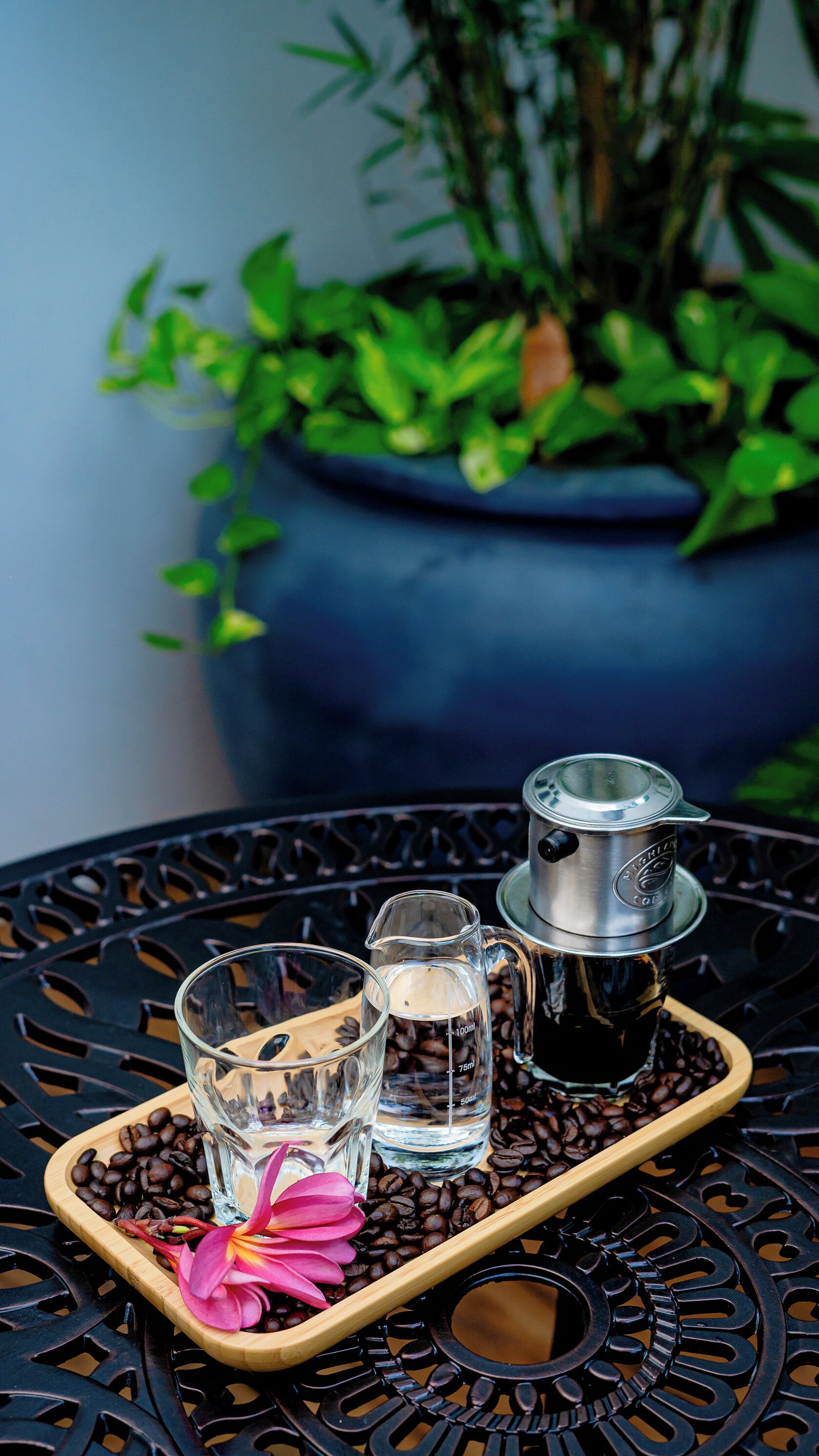 Una bandeja con granos de café, una jarra de agua y un vaso sobre una mesa de metal.