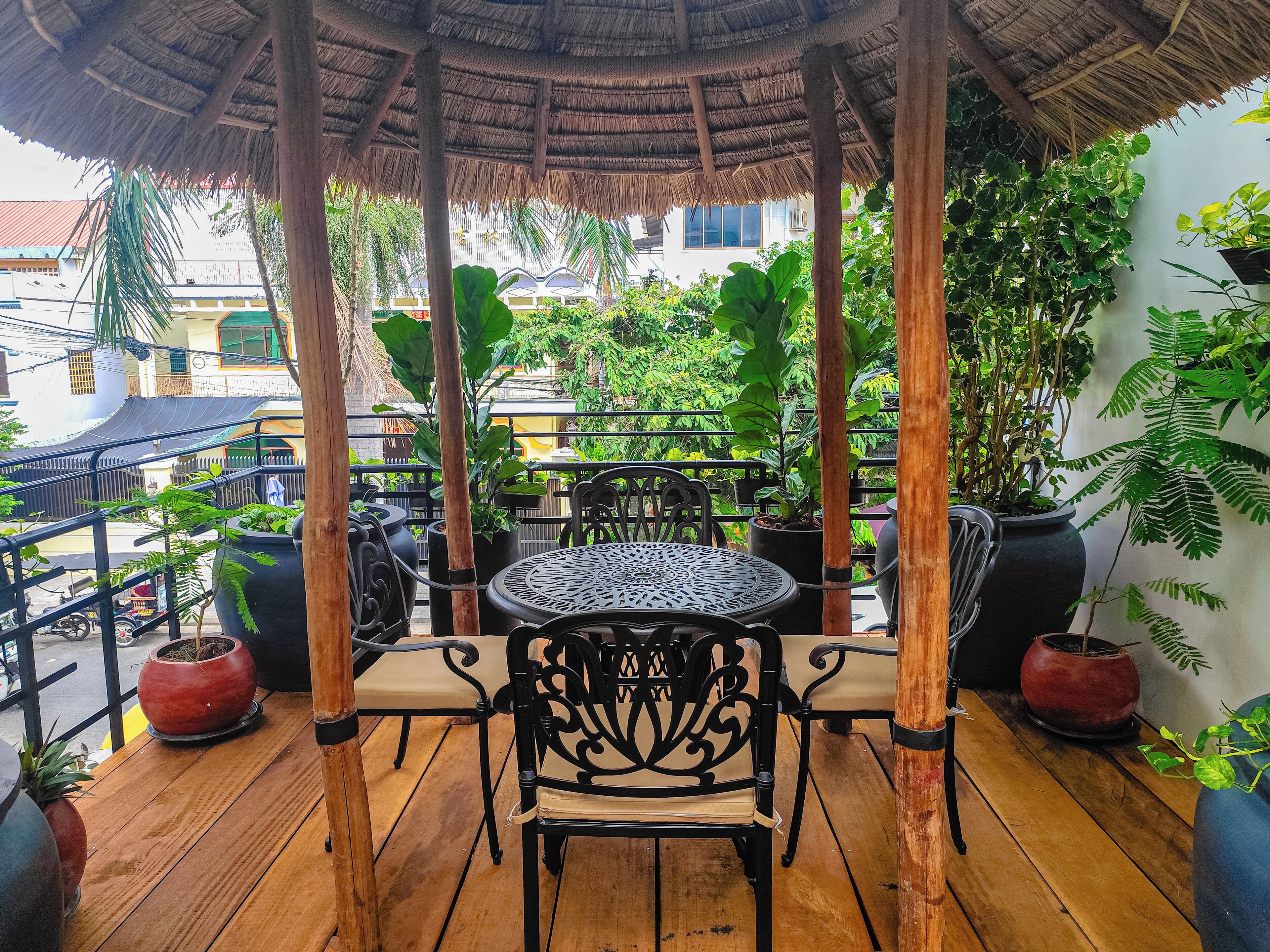 Un espacio al aire libre cubierto con una mesa redonda y sillas, rodeado de macetas con plantas y una terraza de madera.