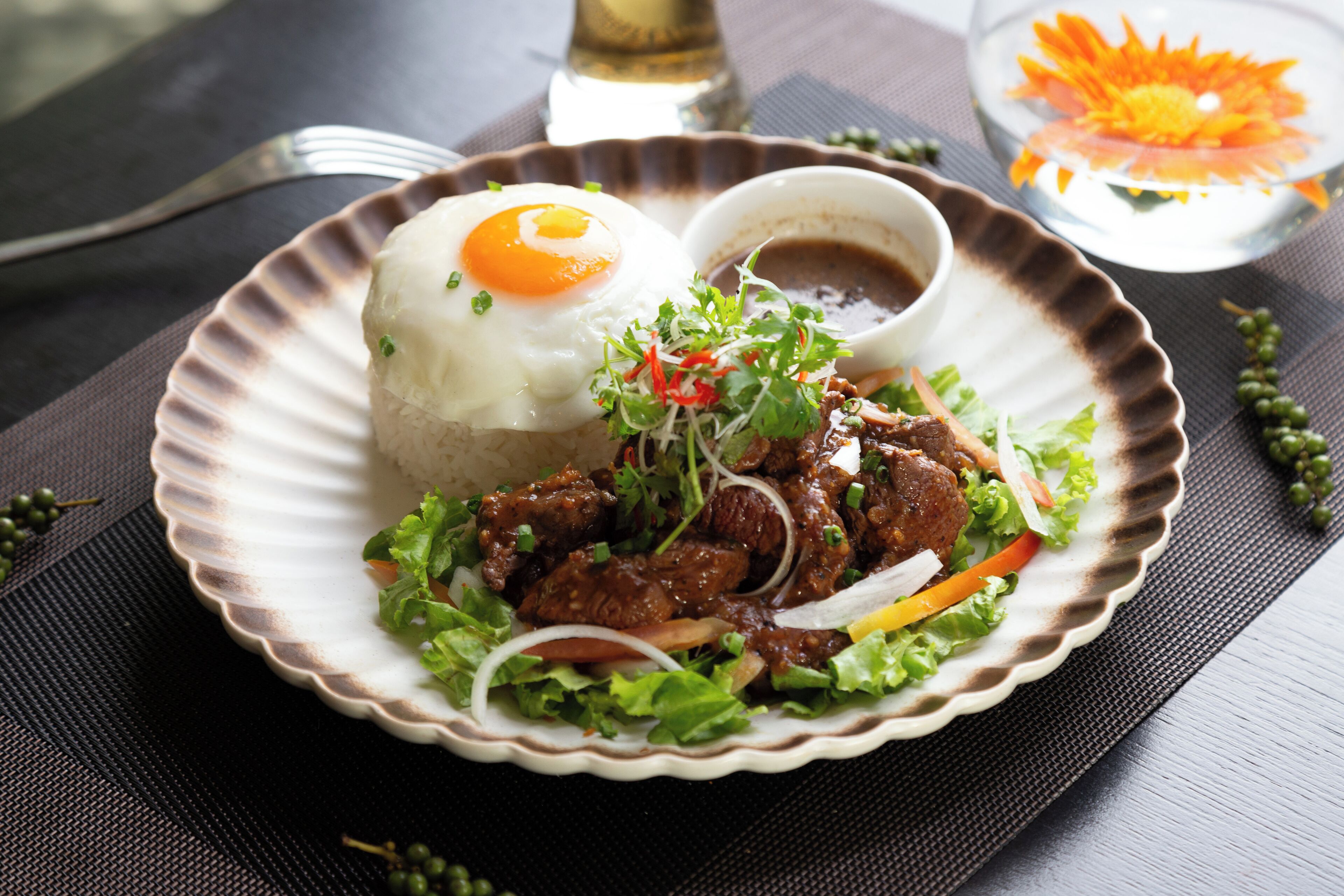 A plate of food with a fried egg, meat, and vegetables, accompanied by a small bowl of sauce.