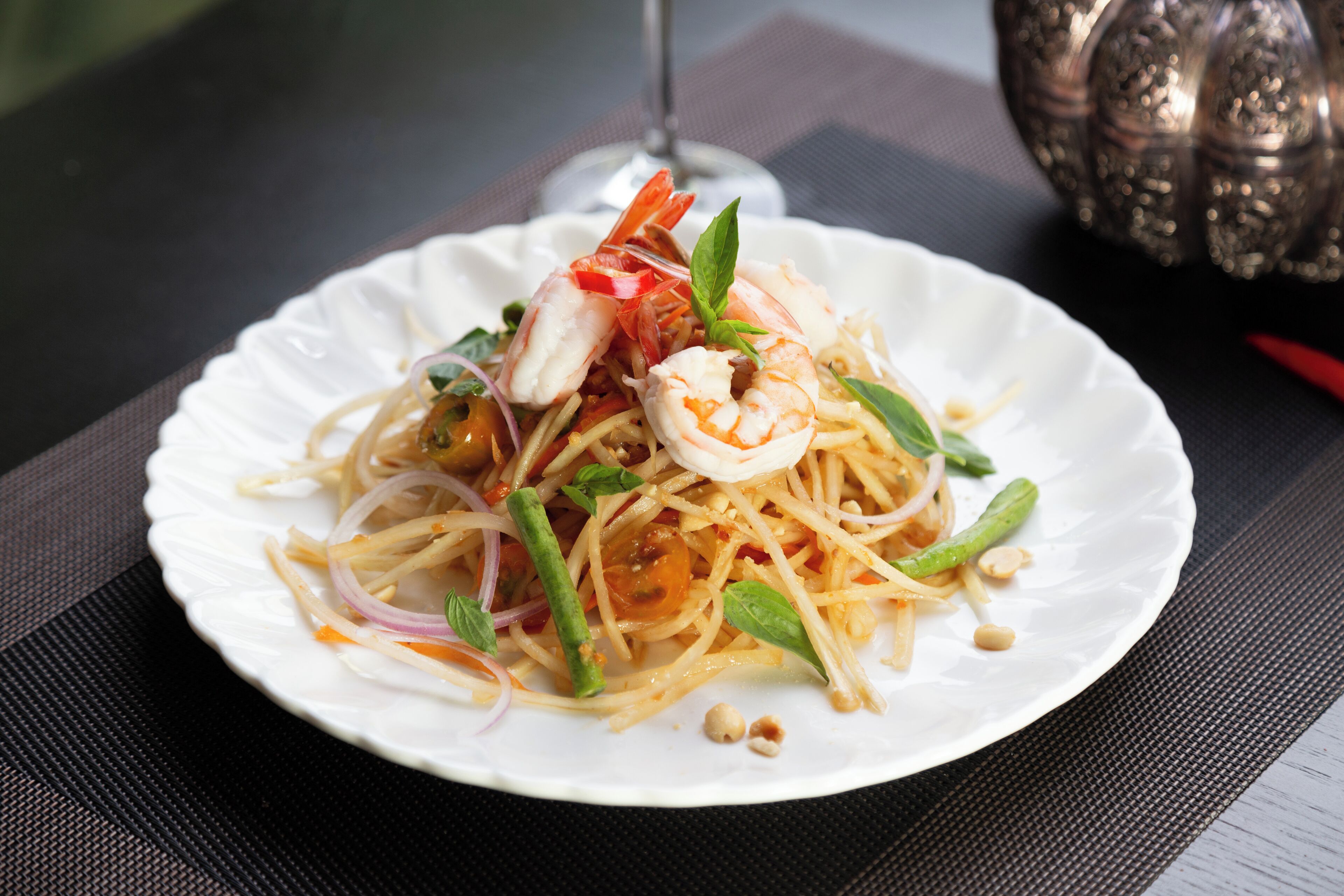 A plate of noodles with shrimp and vegetables on a white plate.