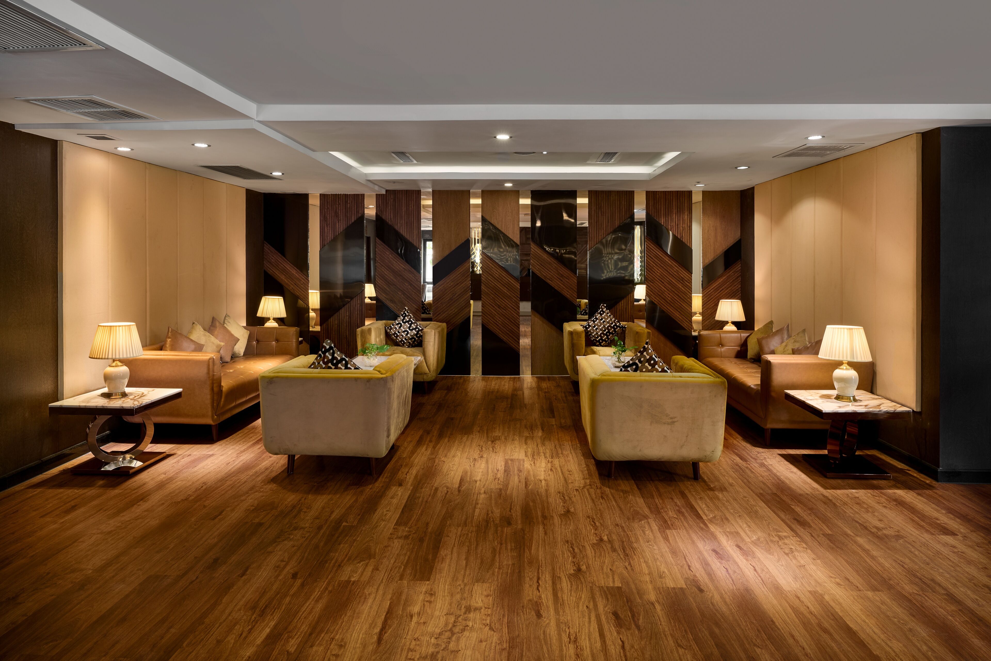 Hall d'albergo dal design moderno, con un'area salotto centrale con divani e poltrone, pavimento in legno e pannelli decorativi alle pareti.