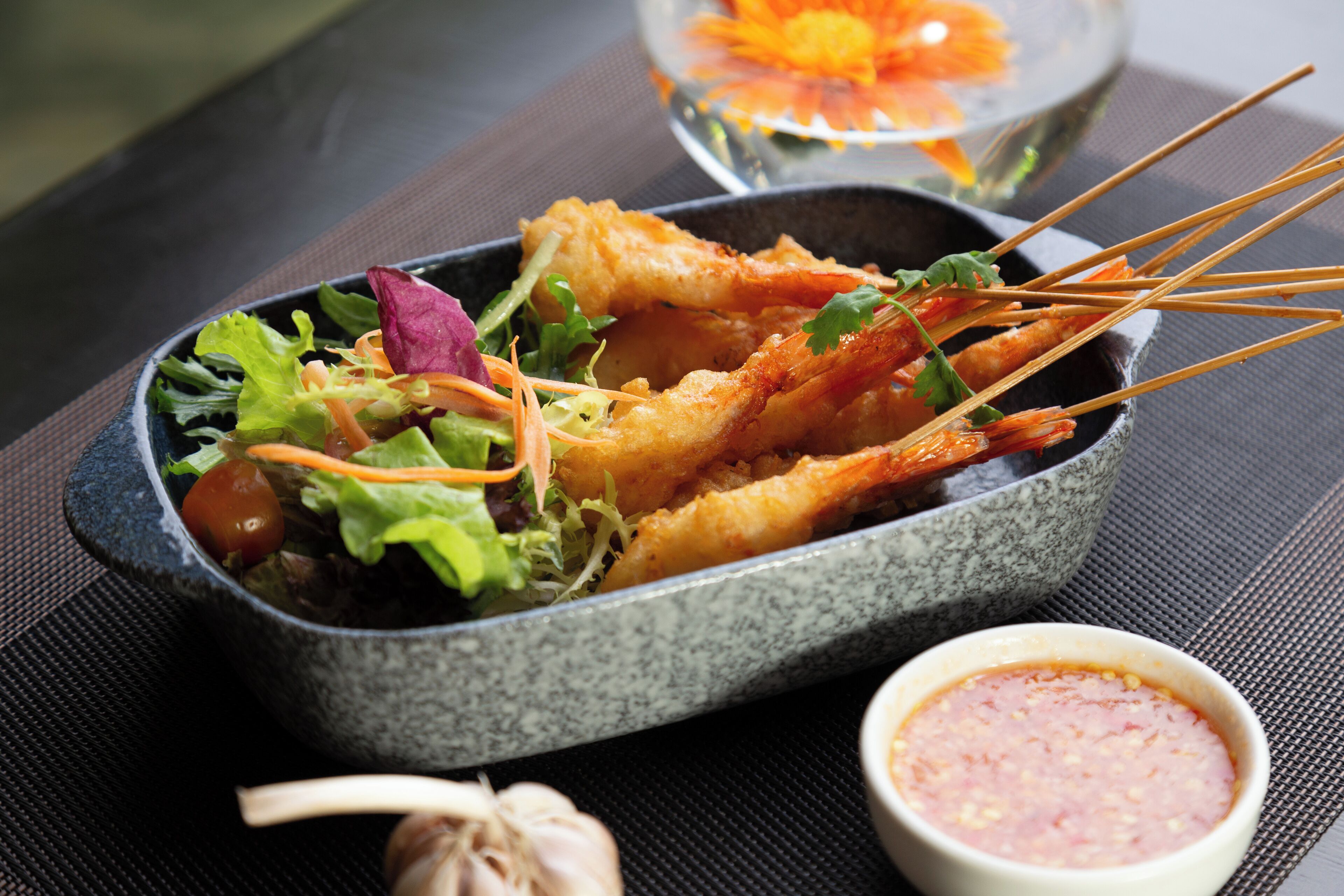 A dish of fried shrimp with vegetables and a dipping sauce on a table.
