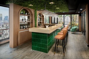 Een moderne bar met een groen betegelde bar, houten planken en een stadszicht door grote ramen.