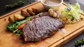 A steak with vegetables and a gravy boat on a wooden board.