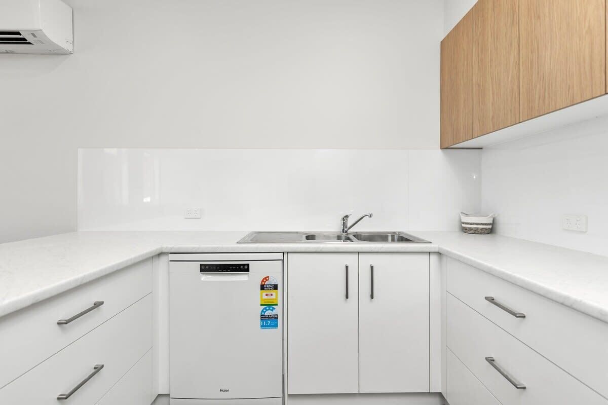 Eine moderne Küche mit weißen Schränken, einem eingebauten Geschirrspüler und einem Holzschrank.