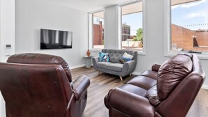 A modern living room with leather sofas, a grey armchair, and a flat-screen TV mounted on the wall.
