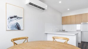 A modern kitchen with white cabinets, a wooden dining table, and a framed bird artwork.
