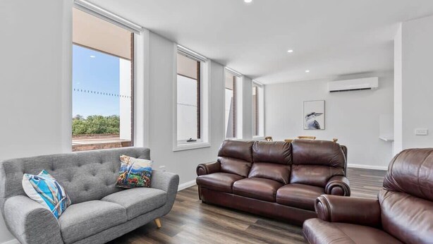 A modern living room with a grey sofa, a brown leather sofa, and a brown leather armchair.
