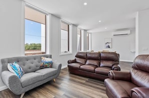 A modern living room with a grey sofa, a brown leather sofa, and a brown leather armchair. - Bedford House - CBD Location, Sleeps 6 (Wagga Wagga)