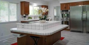 A kitchen with a central island, wooden cabinets, stainless steel appliances, and a window with blinds. - Lupe’s Getaway!! (Fresno)