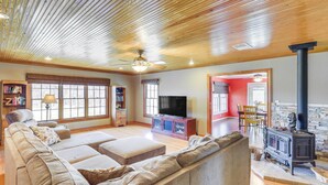 A spacious living room with a large sectional sofa, a flat-screen TV, a fireplace, and a ceiling fan. - Riverside Texas Retreat w/ Wraparound Porch! (Thorndale)