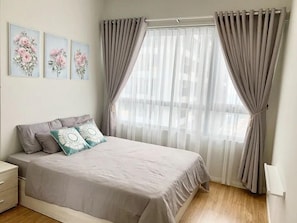 A bedroom with a bed, a nightstand, a dresser, and a window with curtains. - Chiip Apartment in Masteri An Phu  (Ho Chi Minh City)