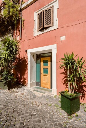 A red building with a wooden door, a window with shutters, and a cobblestone courtyard.