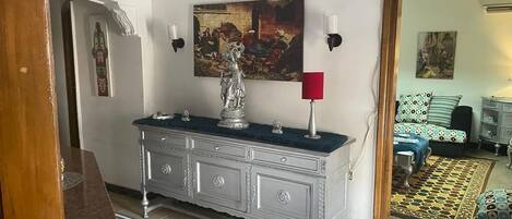Ein Flur mit weißer Wand, einem silbernen Schrank mit dunkler Auflagefläche, einem roten Kerzenhalter und einem Gemälde über dem Schrank.