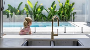 A kitchen with a sink and a view of a swimming pool and plants. - Pool - Ohana - Oceanstays (Yamba)