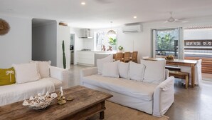 A modern living room with a sofa, coffee table, and dining area. - Pool - Ohana - Oceanstays (Yamba)