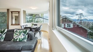 Un salón moderno con sofá, mesa de comedor, sillas y un ventanal con vistas a una casa roja.