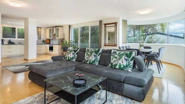 Una sala de estar moderna con un sofá modular, un comedor y una cocina al fondo.