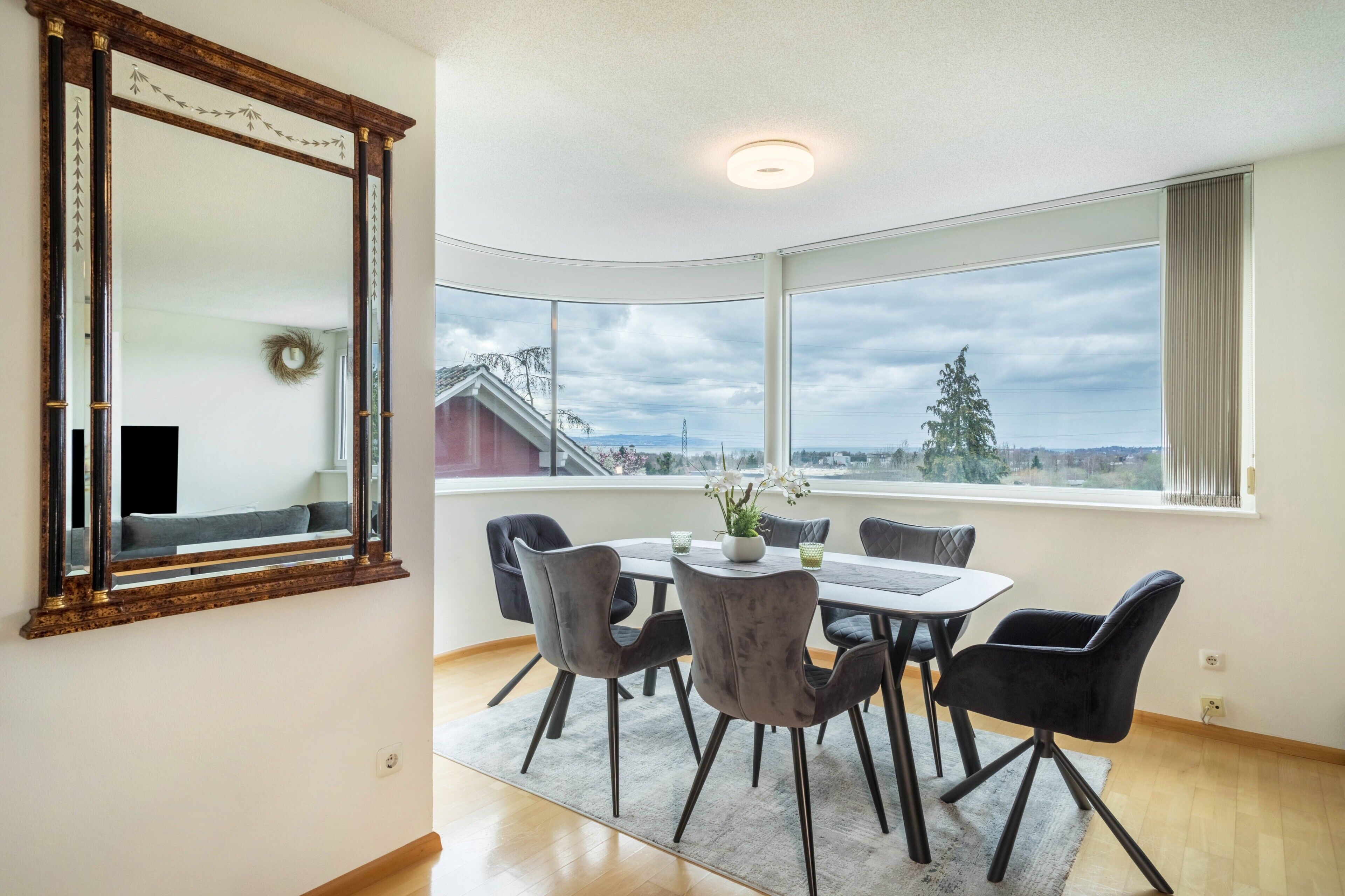 A dining area with a large window, a mirror, and a view of the outside.