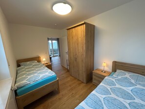 Een slaapkamer met twee bedden, een houten garderobe, een bureau en een balkon.