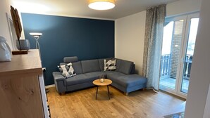 A modern living room with a grey sofa, a small wooden coffee table, and a ceiling light fixture. - Seeblick Holiday Apartment – Ideal for Cycling, Walks, and Relaxation (Versmold)
