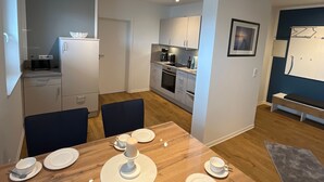 A modern kitchen with white cabinets, a coffee machine, and a dining area with a wooden table set for four. - Seeblick Holiday Apartment – Ideal for Cycling, Walks, and Relaxation (Versmold)
