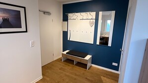 A room with a wooden floor, a bench, a wall-mounted mirror, a framed picture, and a door leading to another room. - Seeblick Holiday Apartment – Ideal for Cycling, Walks, and Relaxation (Versmold)