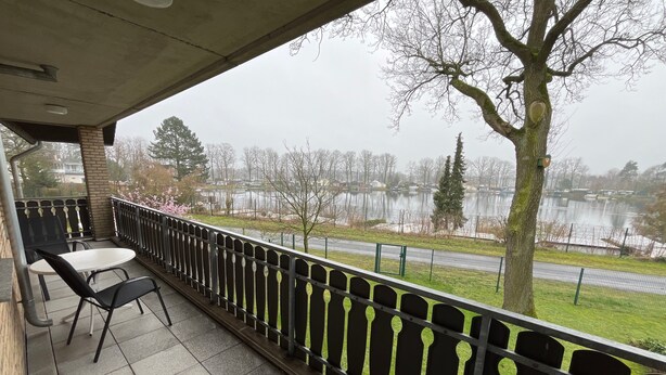 A balcony with a table and chairs, a view of a lake, and a tree. - Seeblick Holiday Apartment – Ideal for Cycling, Walks, and Relaxation (Versmold)