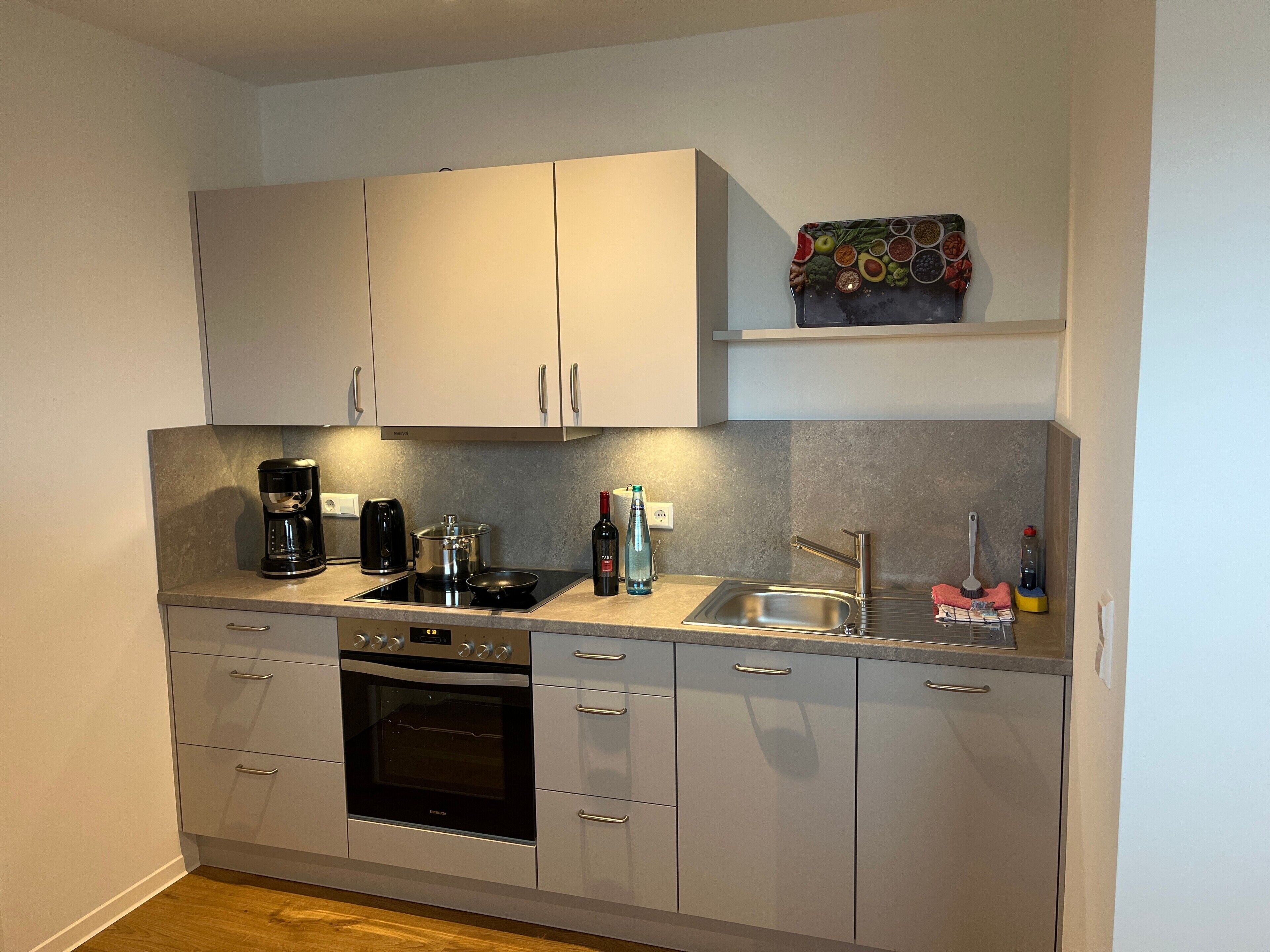 Una cocina compacta con horno integrado, cafetera, hervidor, pileta y especiero.