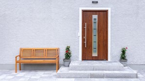 Un banc en bois, une porte en bois avec un panneau de verre et deux plantes en pot.
