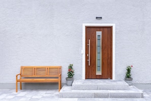 Un banc en bois, une porte en bois avec un panneau de verre et deux plantes en pot.