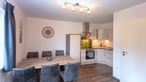 Une cuisine moderne avec des meubles blancs, un four encastré et un coin repas comprenant une table en bois et des chaises grises.