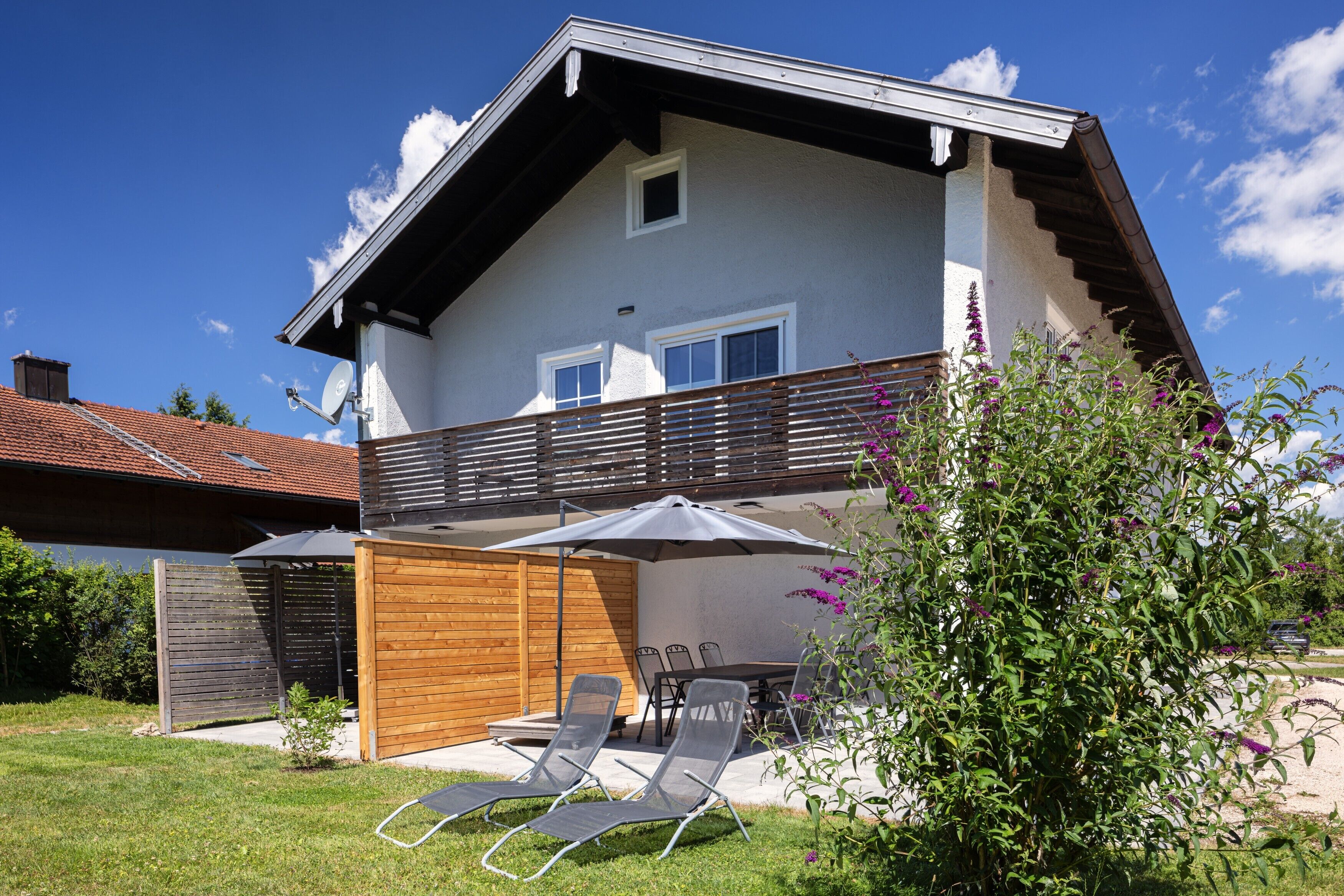 Ein zweistöckiges Haus mit Balkon, Holzzaun und Garten mit Rasen und Sitzgelegenheiten.