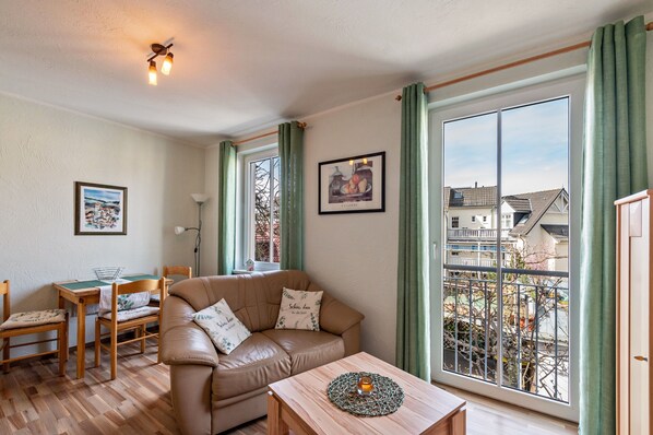 A cozy living room with a leather sofa, wooden coffee table, and a dining area with a table and chairs. - Apartment 'Abendrot' with Wi-Fi (Ostseebad Kühlungsborn)