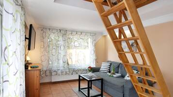Un salon avec un canapé, une petite table, une échelle en bois et une fenêtre ornée de rideaux à motifs.