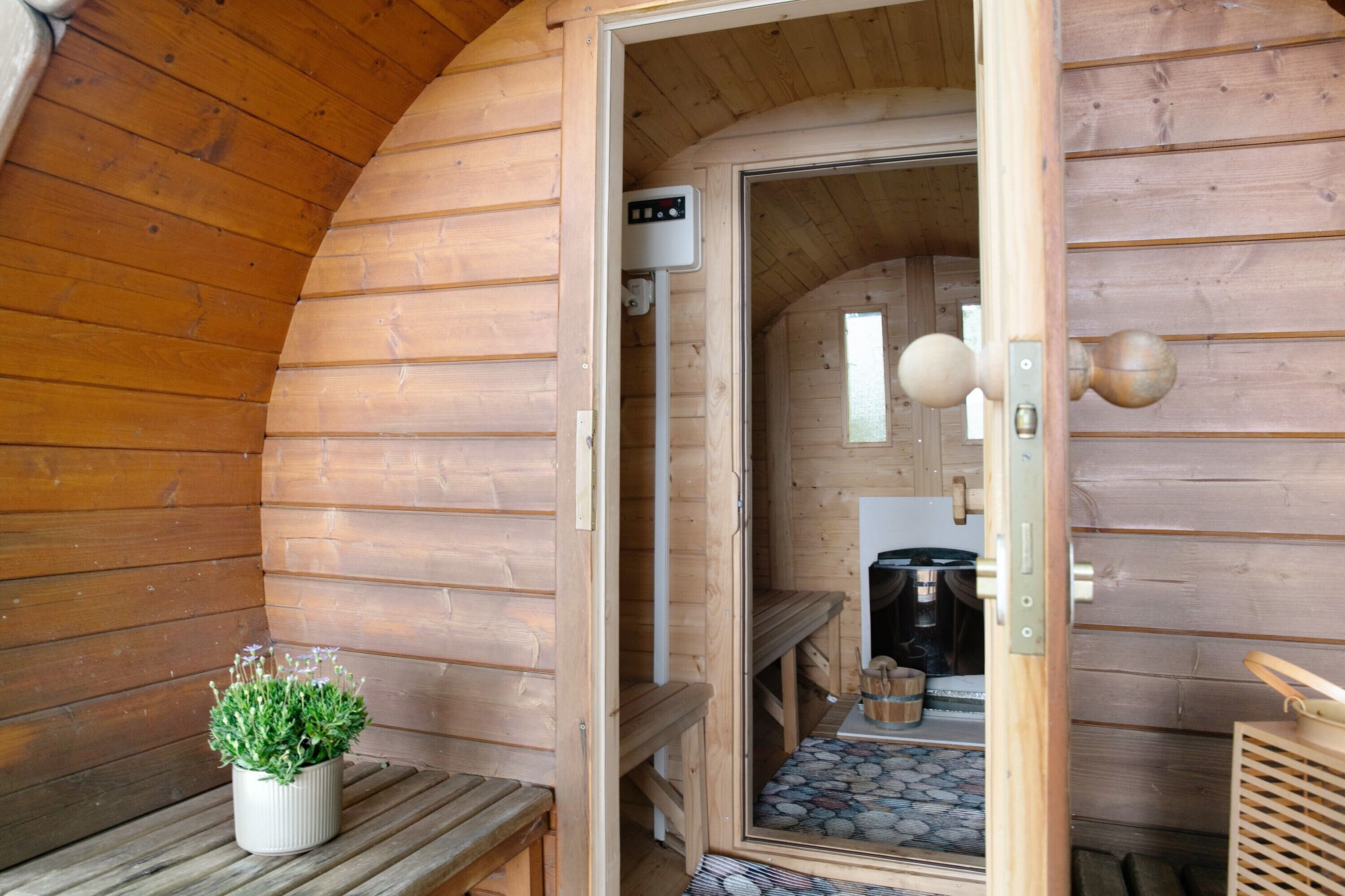 A wooden cabin interior with a bench, a potted plant, a door leading to a kitchen area, and a stone-patterned floor.