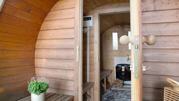 A wooden cabin interior with a bench, a potted plant, a door leading to a kitchen area, and a stone-patterned floor.