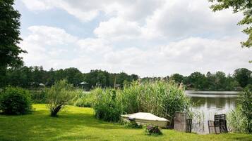 A grassy area with a boat and chairs near a lake, surrounded by trees and vegetation.