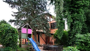A playground with a slide, surrounded by greenery and a building with multiple windows. - Lakefront Holiday Cottage with Private Terrace and Wi-Fi (Bestensee)