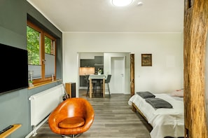A modern room with a bed, a chair, a TV, a table, and a kitchen area.