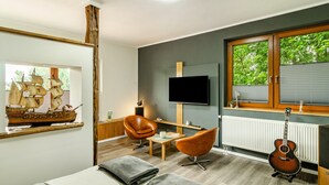 A modern living room with a wooden ship model, a television, a guitar, and a window with blinds.