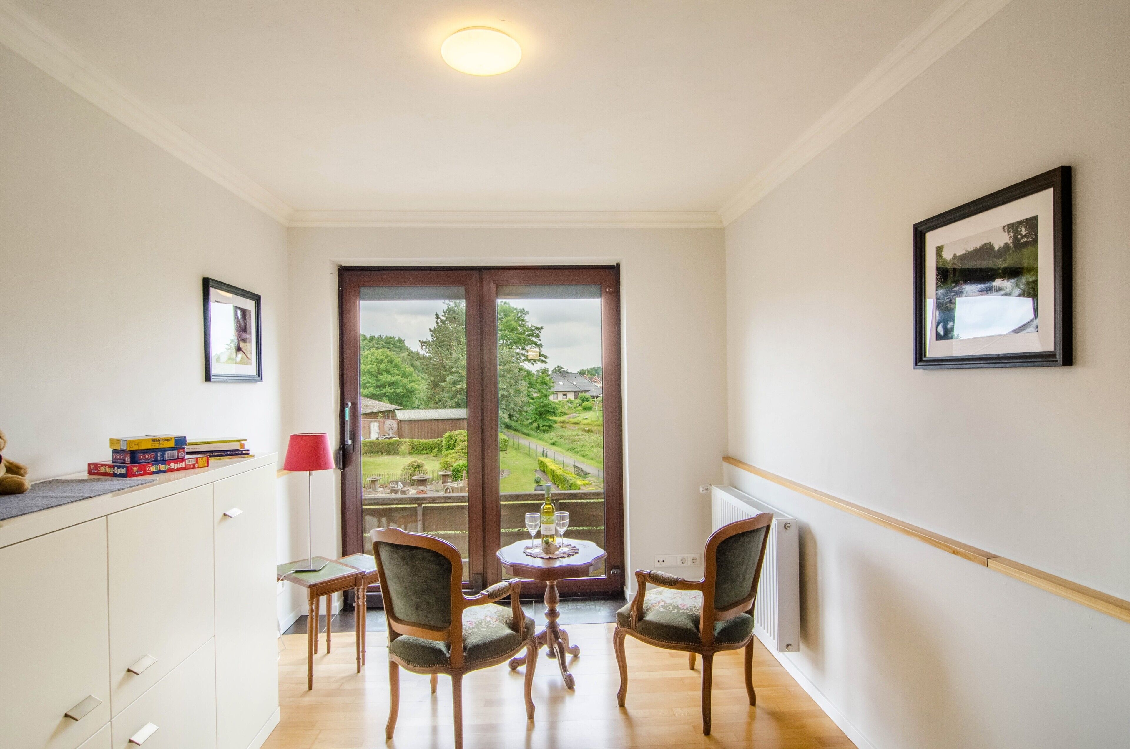 Una habitación con balcón, una mesa de comedor con sillas, un radiador y vistas a la vegetación.