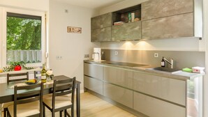 A modern kitchen with a dining table, chairs, and a window with greenery outside. - Apartment 'Fewo2 Seelter Uutkiek Saterland' with Private Terrace, Shared Garden and Wi-Fi (Saterland)