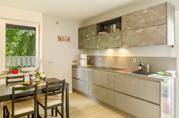 A modern kitchen with a dining table, chairs, and a window with greenery outside.