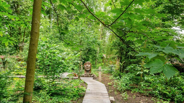 A wooden pathway in a forested area with dense greenery and a large stone sculpture. - Apartment 'Fewo2 Seelter Uutkiek Saterland' with Private Terrace, Shared Garden and Wi-Fi (Saterland)