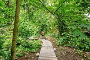 A wooden pathway in a forested area with dense greenery and a large stone sculpture. - Apartment 'Fewo2 Seelter Uutkiek Saterland' with Private Terrace, Shared Garden and Wi-Fi (Saterland)