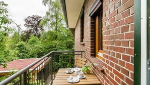 A balcony with a table set for two, a brick wall, and a view of lush greenery. - Apartment 'Fewo2 Seelter Uutkiek Saterland' with Private Terrace, Shared Garden and Wi-Fi (Saterland)