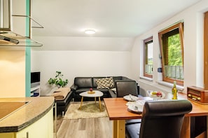 A compact living space with a kitchenette, a dining area, a sofa, and a window with a view of greenery.