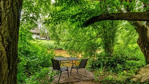 Eine Holzterrasse mit Tisch und Stühlen, umgeben von üppigem Grün und Bäumen.